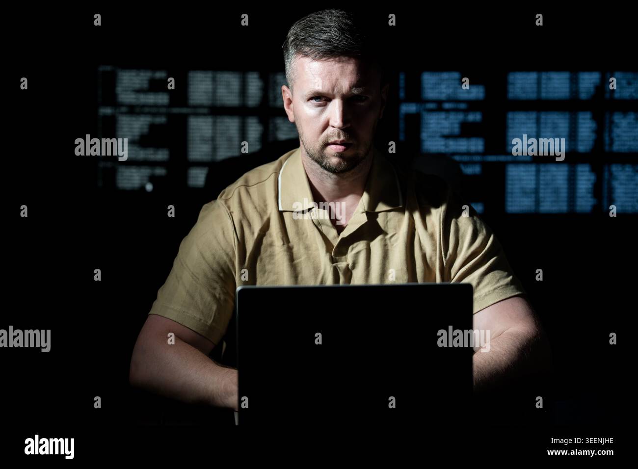 Hacker works late in dark room. Hacker analyzes software and programming code. Hacker monitors secure server system. Hacker creates ransomware attack Stock Photo