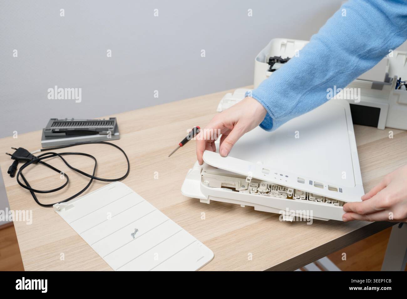 Hands of a technician disassembling a flatbed scanner printer on a wooden desk with tools, cables and spare parts, illustrating office equipment repai Stock Photo