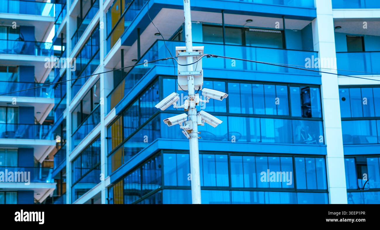 Multiple security cameras on a pole against a modern blue glass building Stock Photo