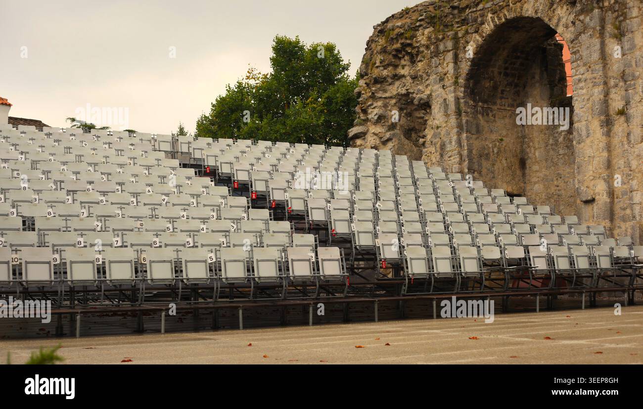 Empty white rows of seats in the Crekvina outdoor amphitheater in Kastav, Croatia. Historic ancient stone arch and ruins in the background. Stock Photo