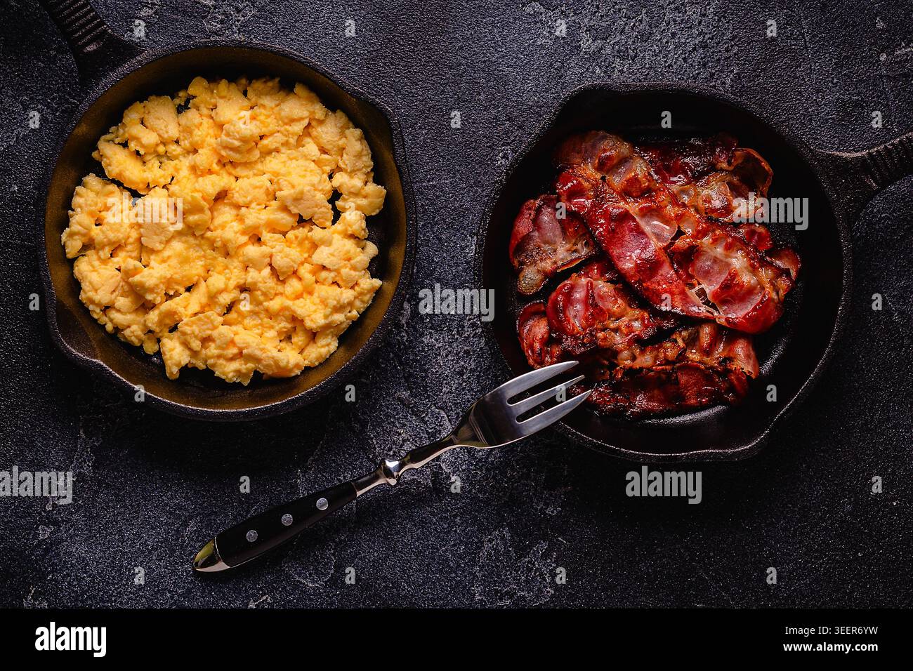 Cooked scrambled eggs and fried bacon in portion pans, top view. Stock Photo