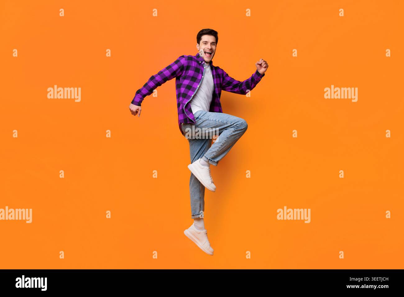 Young Man Jumping Against Bright Orange Background Having Fun Stock Photo