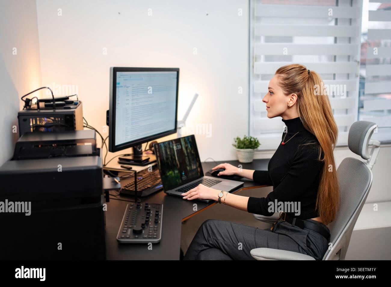 Young adult woman programming on laptop and monitor in modern home office Stock Photo