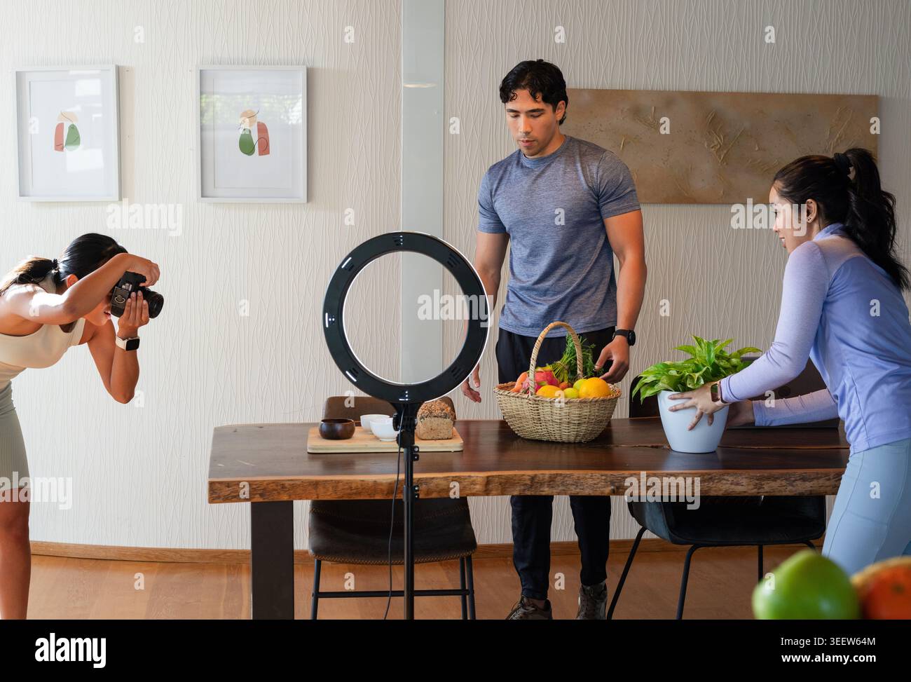 Diverse photography team arranging fruit basket on wooden dining table with LED ring, DSLR camera Stock Photo
