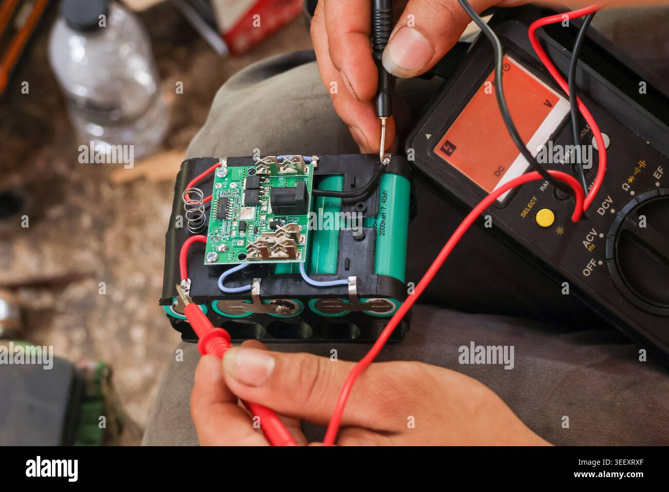 Focused technician hand using digital multimeter tool testing battery pack circuit board repair process measuring voltage current electronics hardware Stock Photo