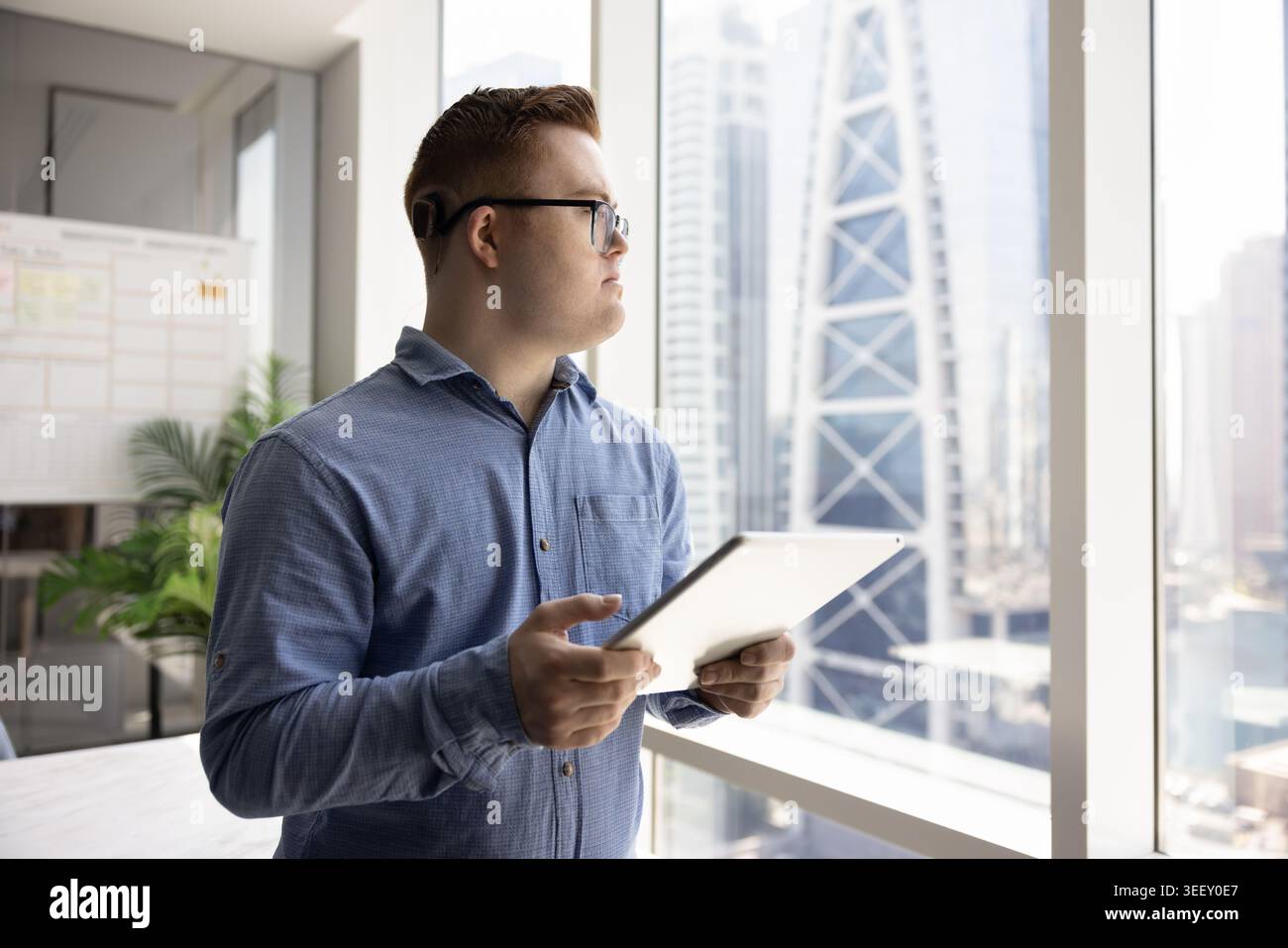 Thoughtful man with Down syndrome working on tablet in office Stock Photo
