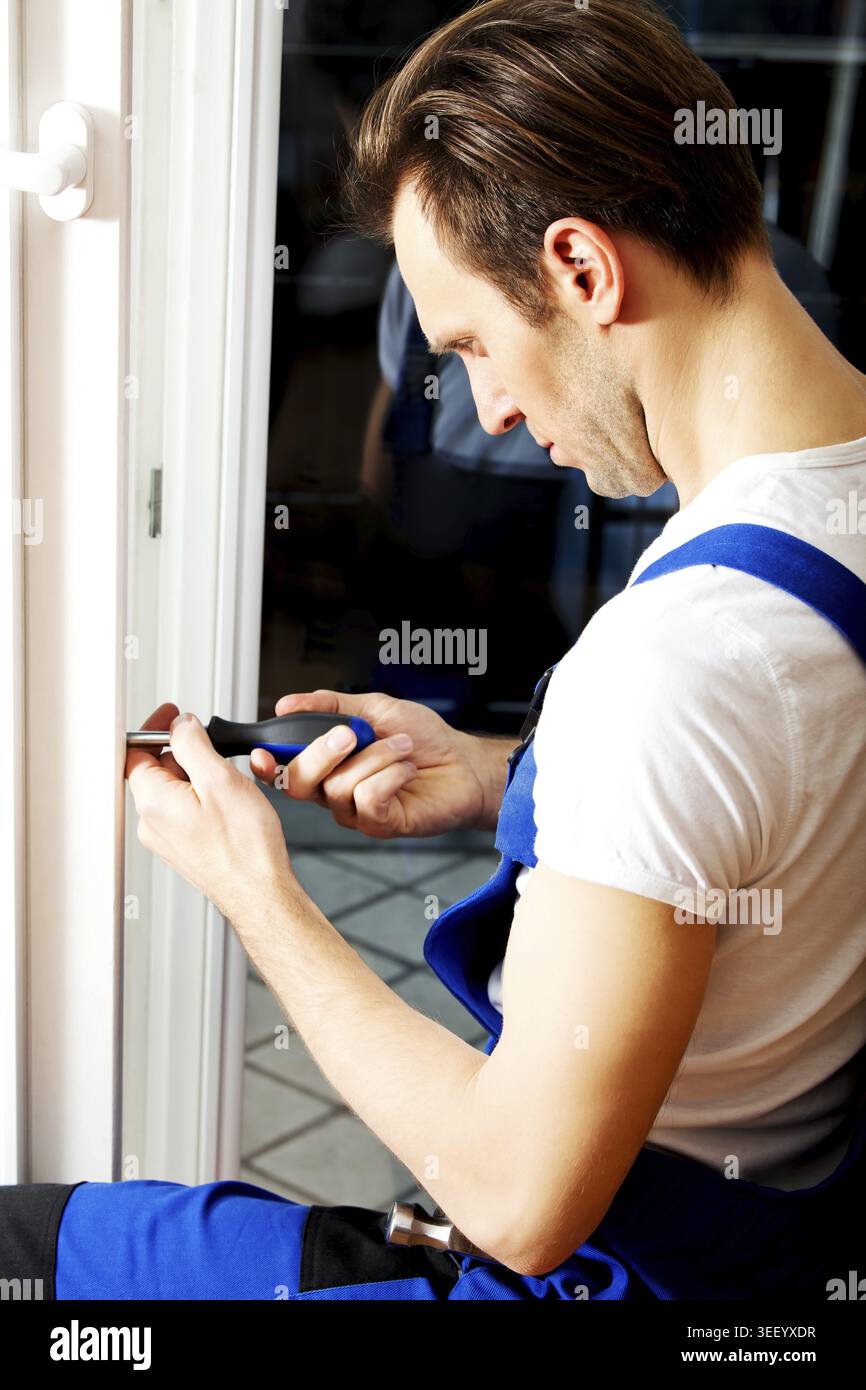 Young handyman repair window with screwdriver Stock Photo