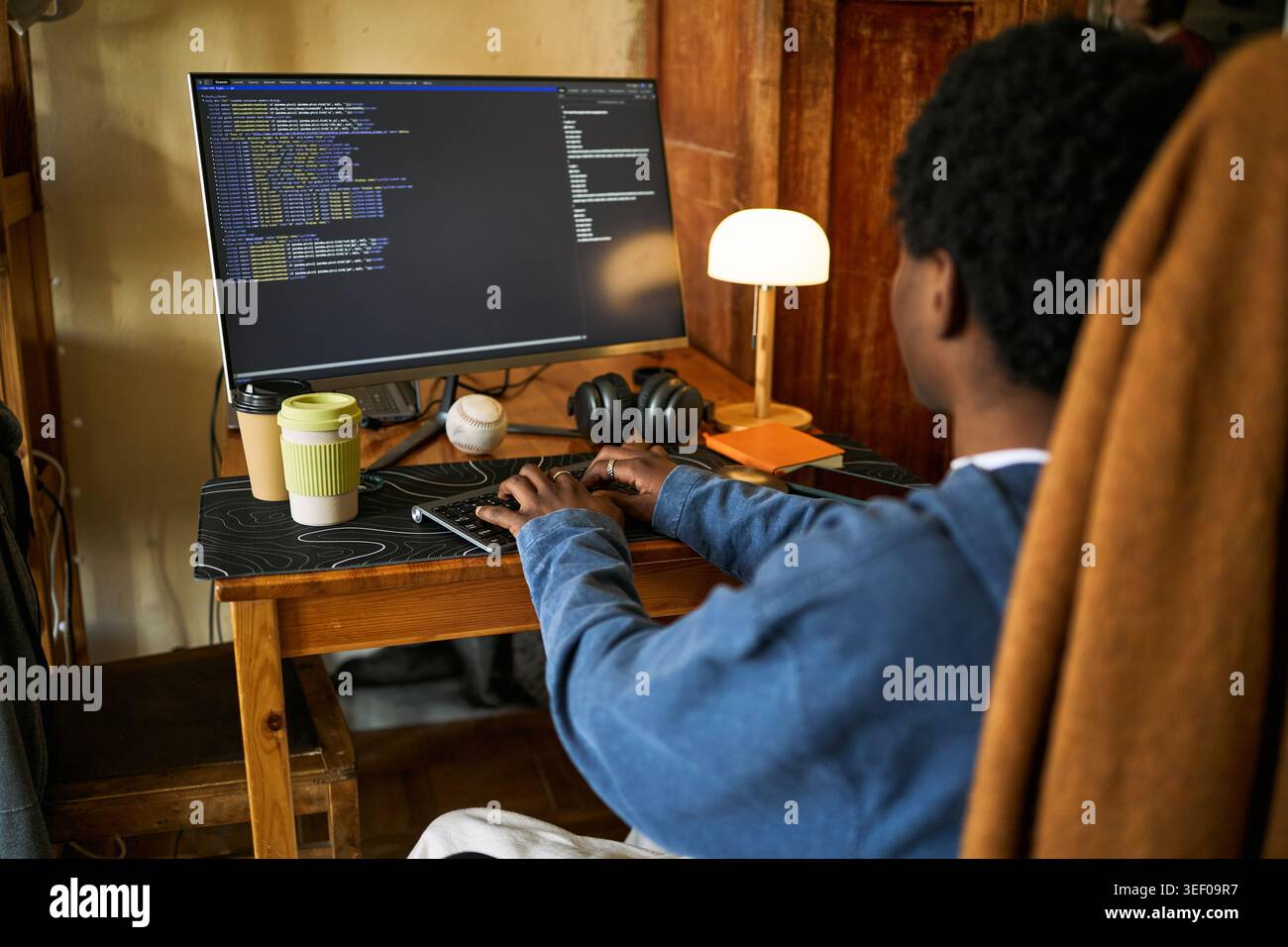 Young Black man coding at desktop computer in home office, typing software script for remote work and digital development. Ideal for tech careers, programming, freelance business Stock Photo