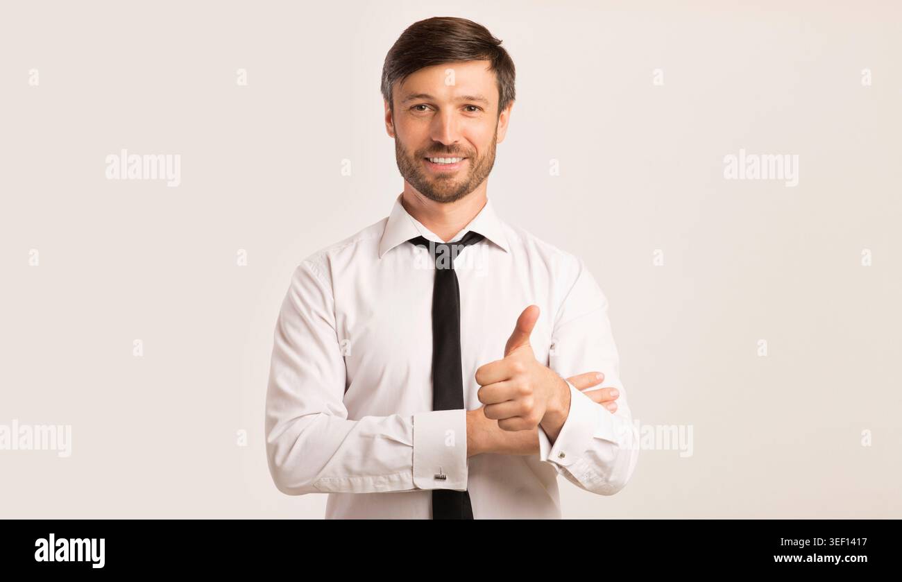 Businessman Gesturing Thumbs Up Smiling At Camera, Isolated, Studio Shot Stock Photo