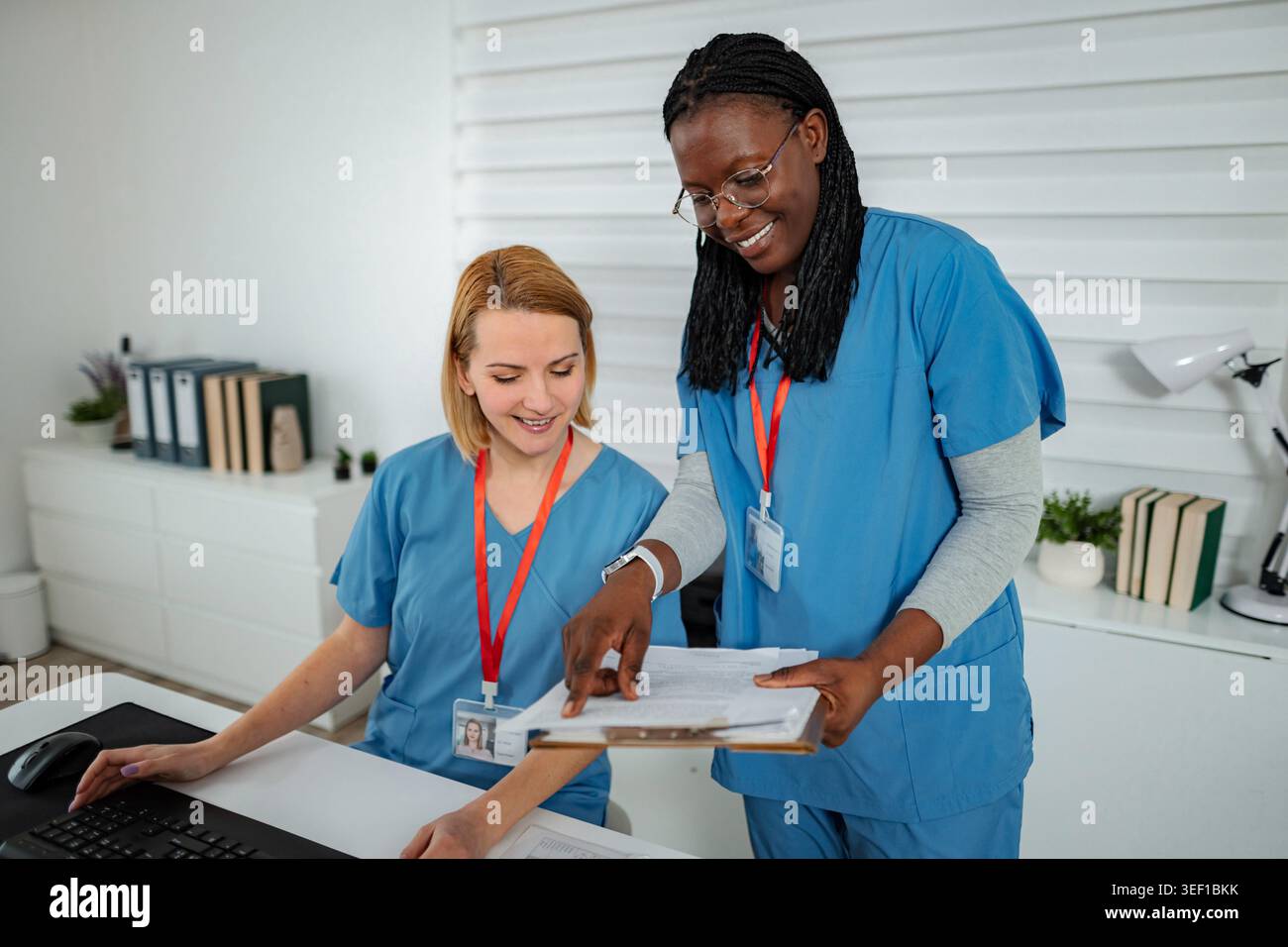 Two nurses are discussing patient records and using a computer in a clinical setting Stock Photo