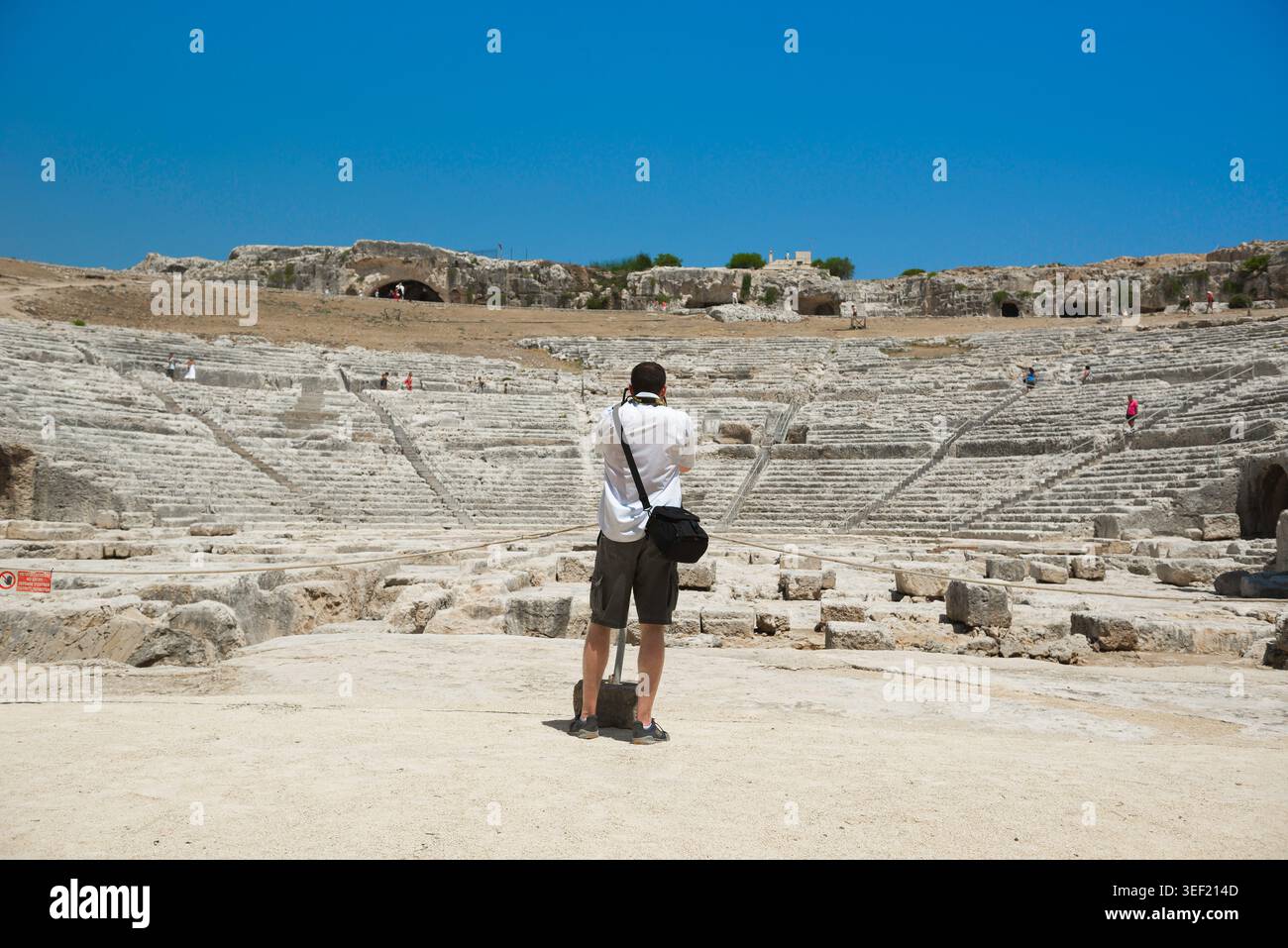 Travel Europe, rear view of a solo male photographer taking a photo of the ancient Greek Theater sited in the Archaeological Park in Siracusa, Sicily Stock Photo
