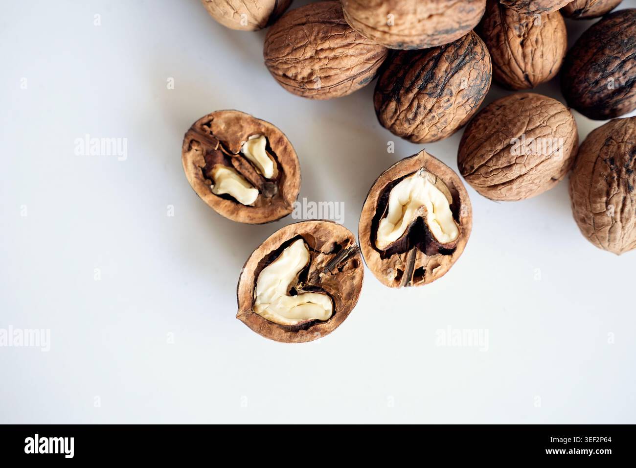 Cracked walnut halves with whole nuts on white background. Stock Photo