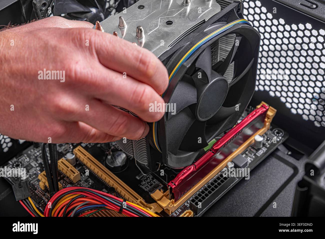 A person's hand is shown installing CPU cooler onto a motherboard inside a desktop computer case. Stock Photo