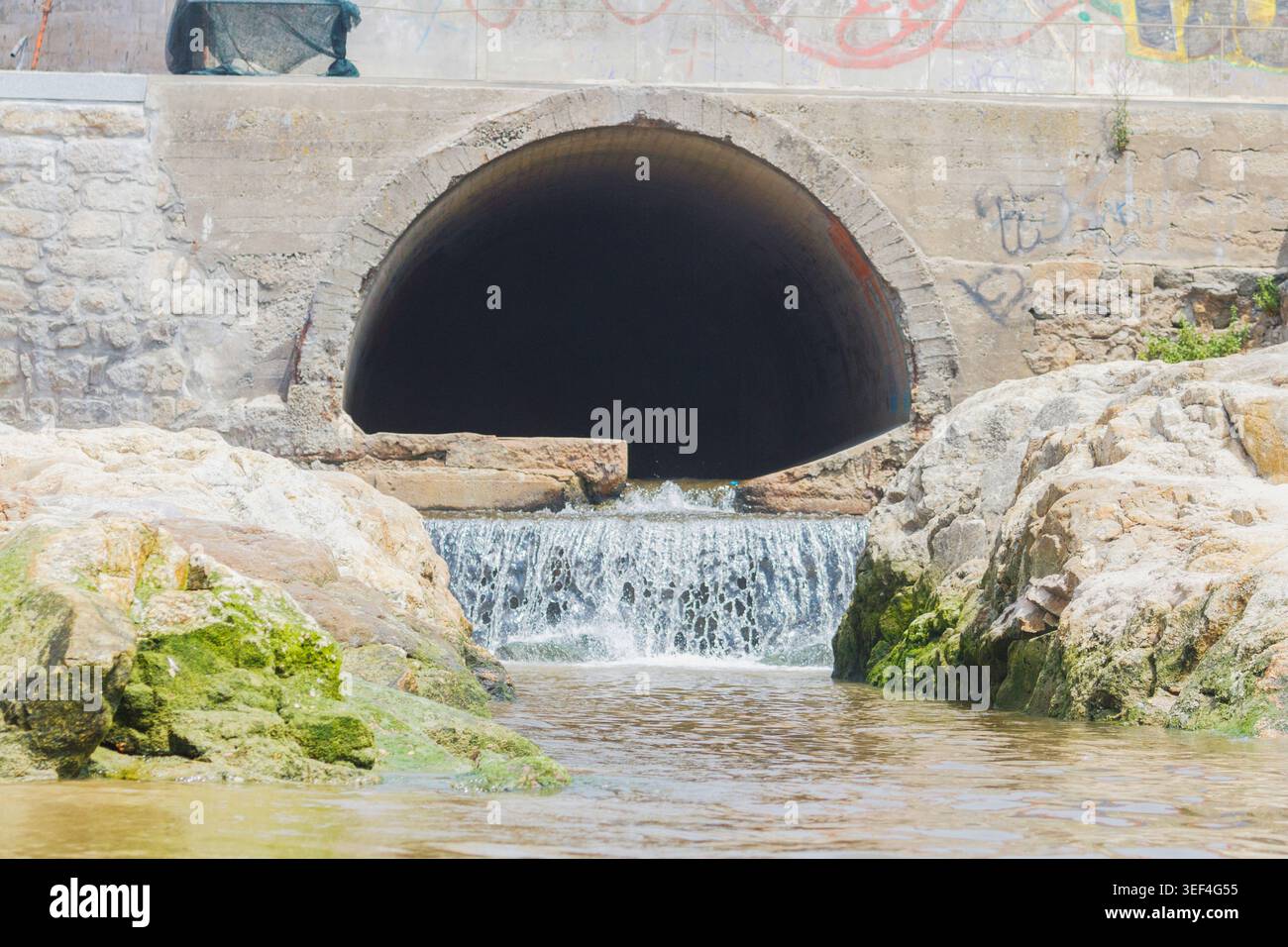 An old, weathered concrete culvert releasing water into a natural rocky ...