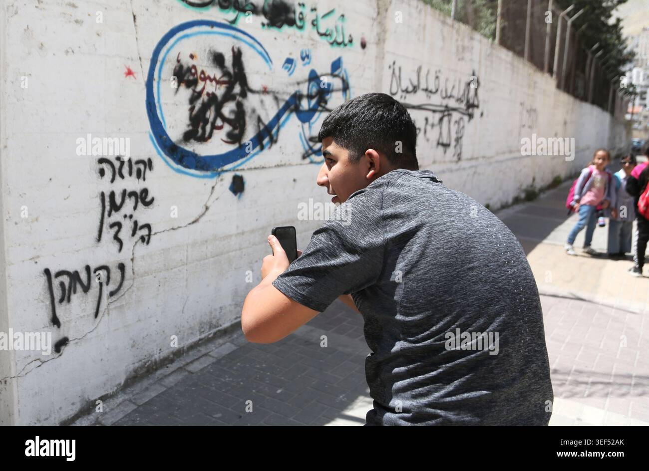 Nablus, Palestine. 13th May, 2026. A Palestinian student takes a photo with his mobile phone of Hebrew graffiti and an Israeli Star of David painted by Jewish settlers on the wall of a Palestinian school in the West Bank city of Nablus. The graffiti was painted by a group of religious Jewish settlers during Talmudic prayers at Joseph's Tomb in Nablus. Credit: SOPA Images Limited/Alamy Live News Stock Photo