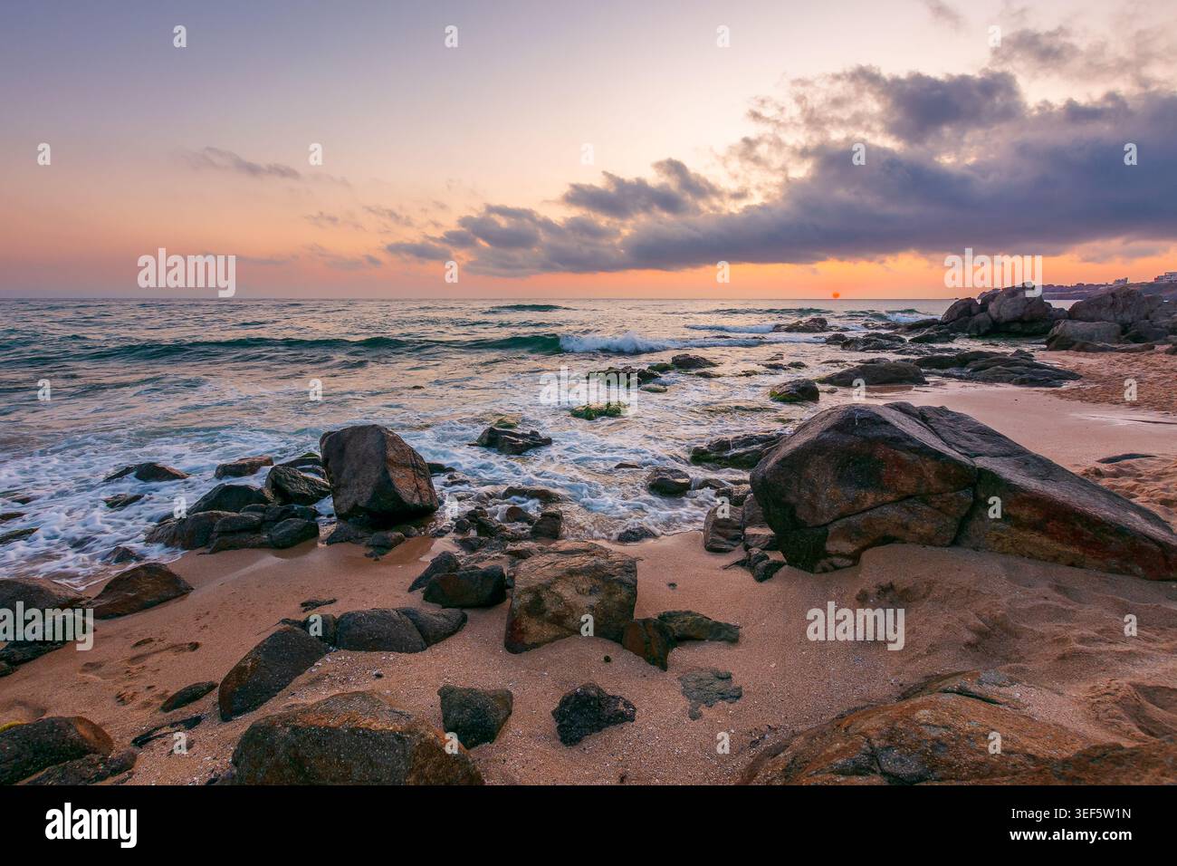 huge stones on a sandy beach at sunrise. wonderful summer vacation season at the black sea. calm waves washing the sand shore. nature background with Stock Photo
