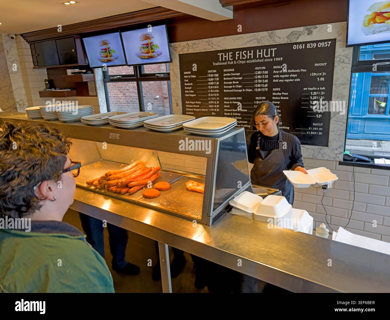 Interior of The Fish Hut fish and chip shop on Liverpool Road, Manchester, showing staff serving customers at the counter Stock Photo