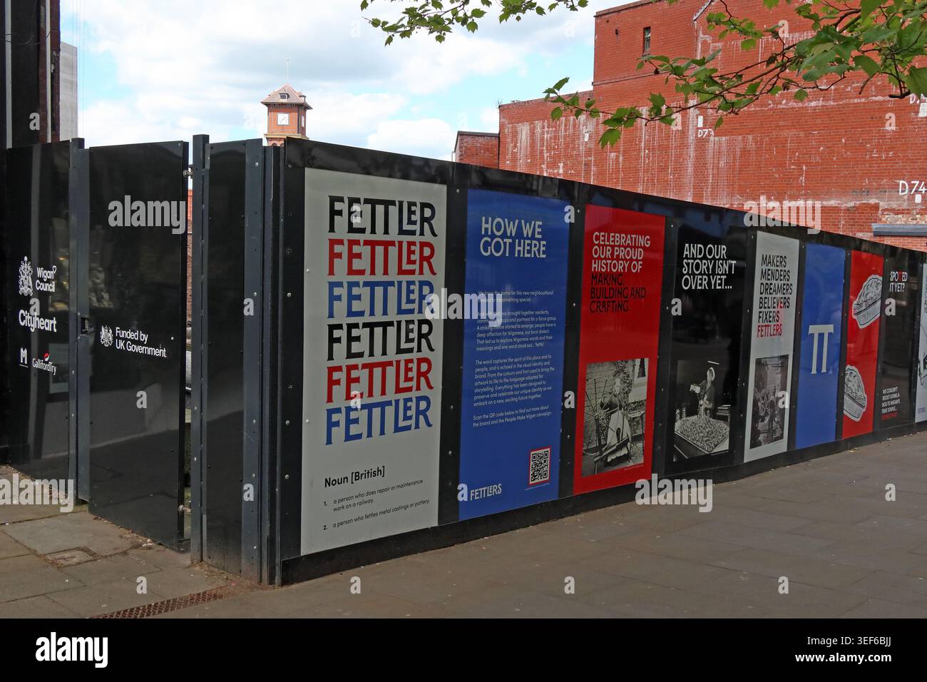 Construction hoardings for Wigan’s Fettlers shopping centre development, celebrating local building and factory work heritage. Stock Photo