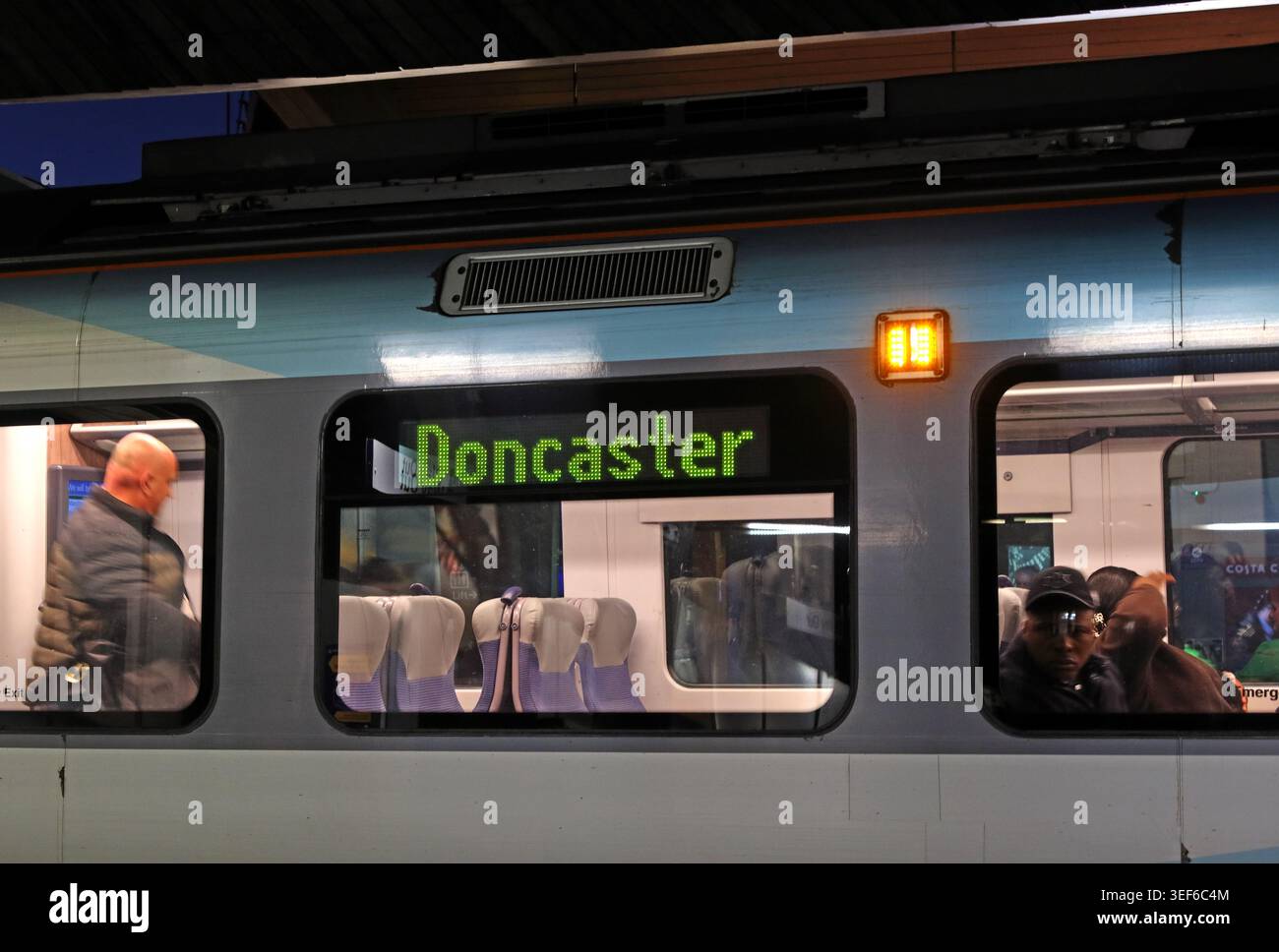 TransPennine Express train showing Doncaster destination at dusk, with passengers visible through lit carriage windows, UK Stock Photo
