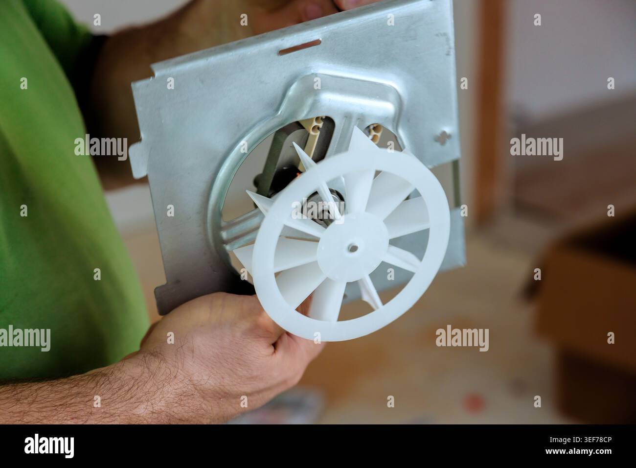 Worker holds fan motor assembly while working on it in home workshop setting. Stock Photo