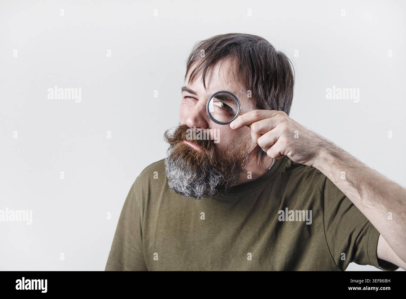 Curious bearded man see through magnifying glass. Science and curiosity concept Stock Photo