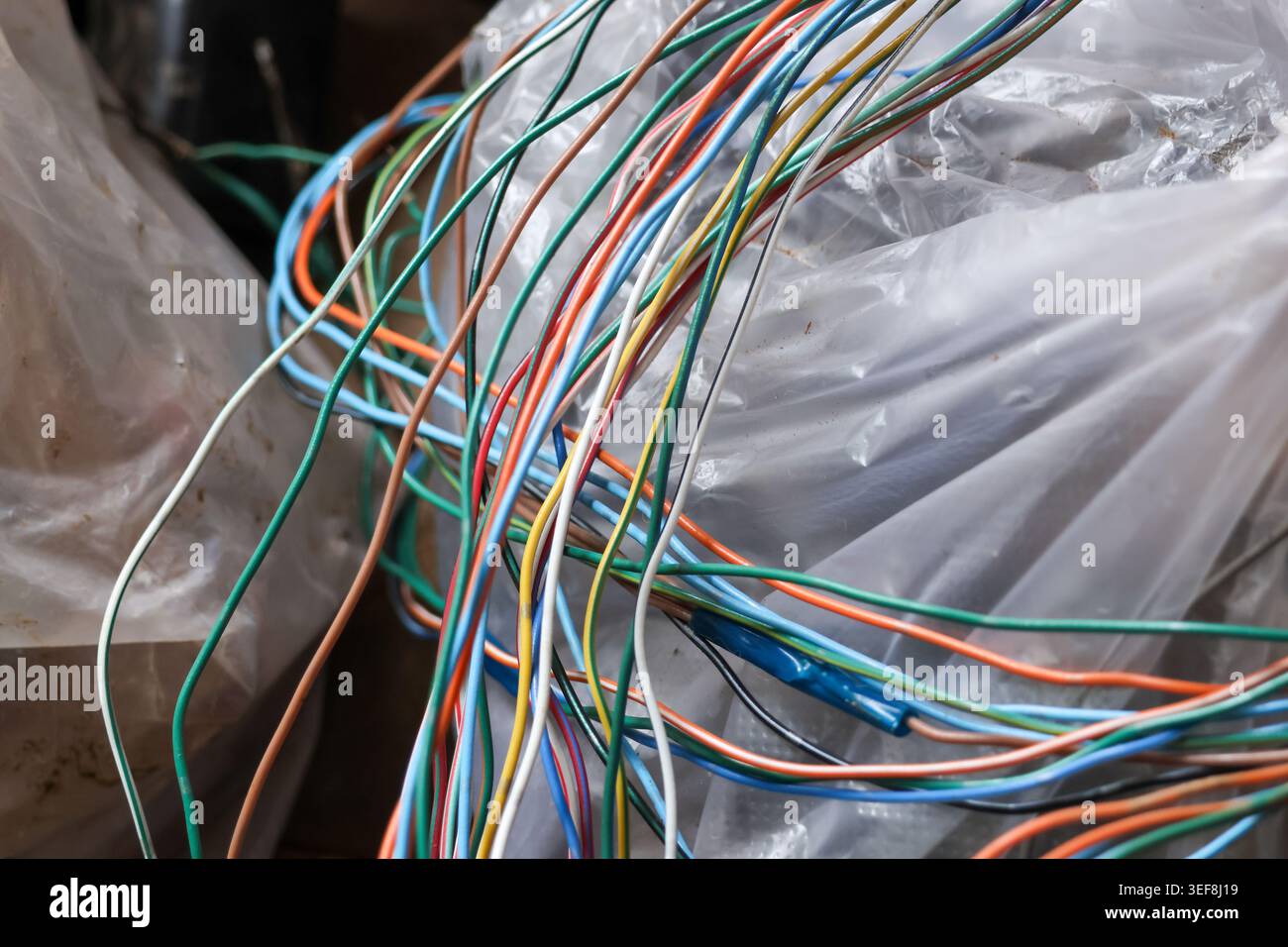 Tangled bundle of colorful electrical wire and cable resting on clear plastic wrap representing chaotic frustrating technology connection and complex Stock Photo