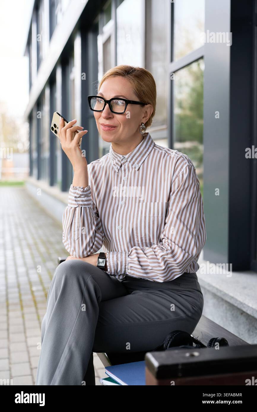 Sophisticated adult woman engages in a pleasant phone conversation while sitting outside. Stock Photo