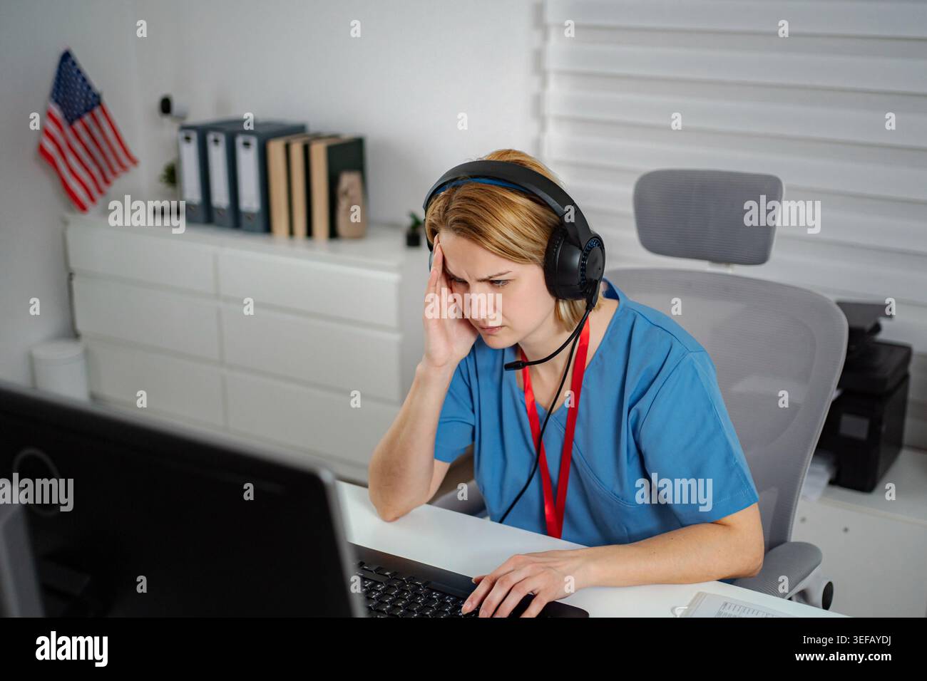 Stressed medical professional working on computer with headset Stock Photo