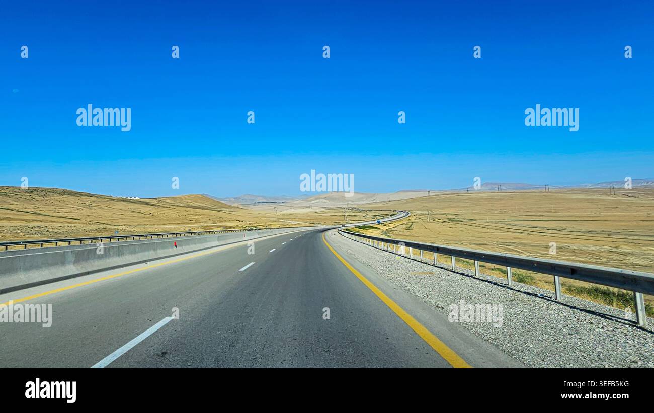 Long and winding road stretches through arid landscape in Northern Azerbaijan under clear blue sky Stock Photo
