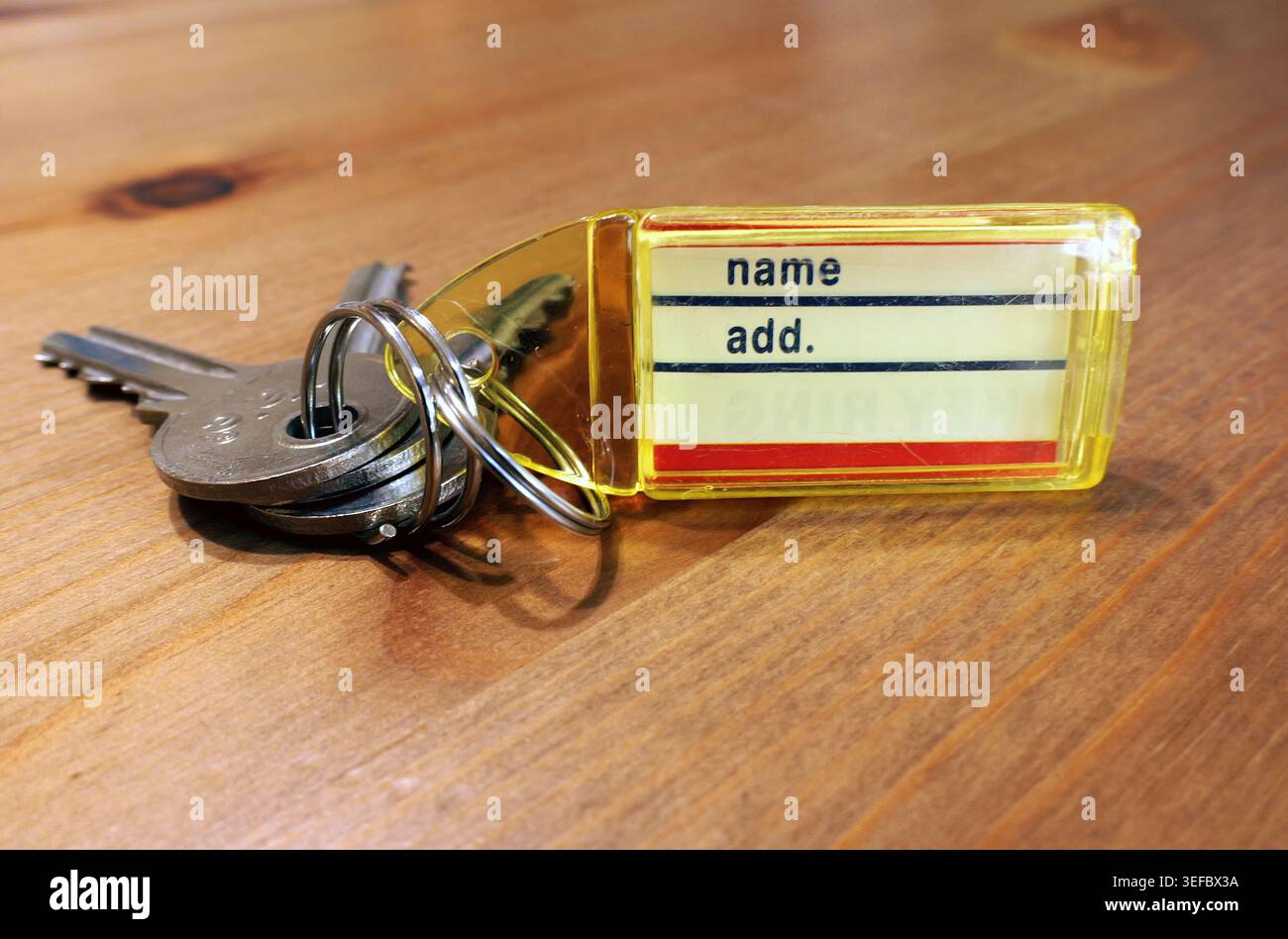 Metal keys on a ring with a yellow transparent keychain showing name and add. Lines, resting on a textured wooden table, symbolizing security, ownersh Stock Photo