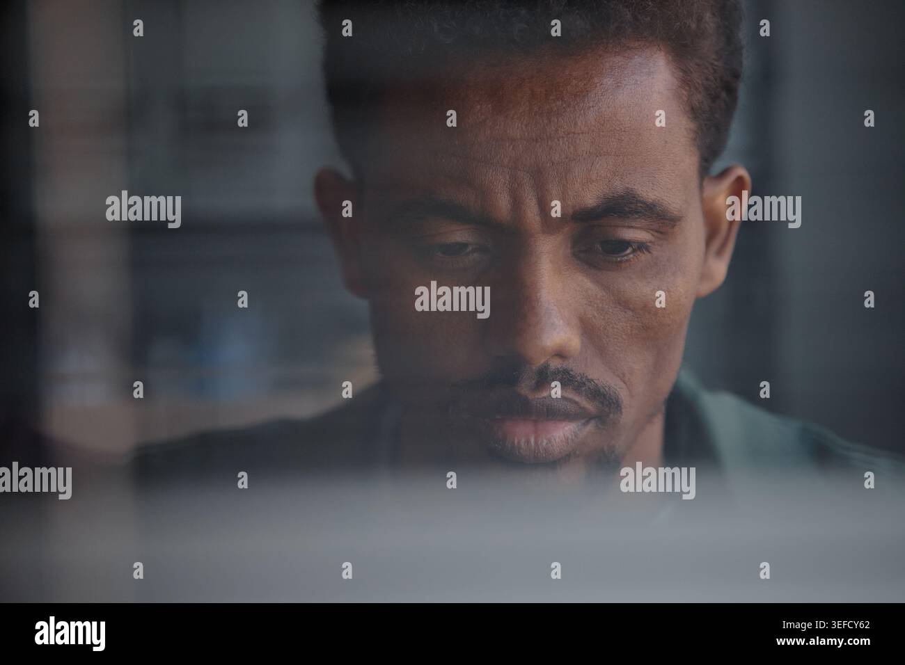 Black Man Working on Laptop through Window in Remote Work Setting Stock Photo