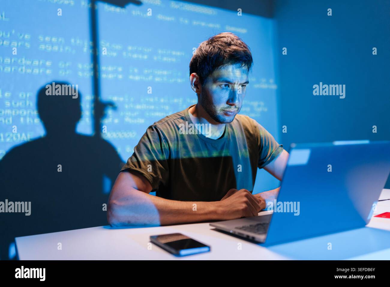 Focused programmer concentrating on laptop, debugging code with projected lines on wall background, developing new software, working late in dark tech Stock Photo