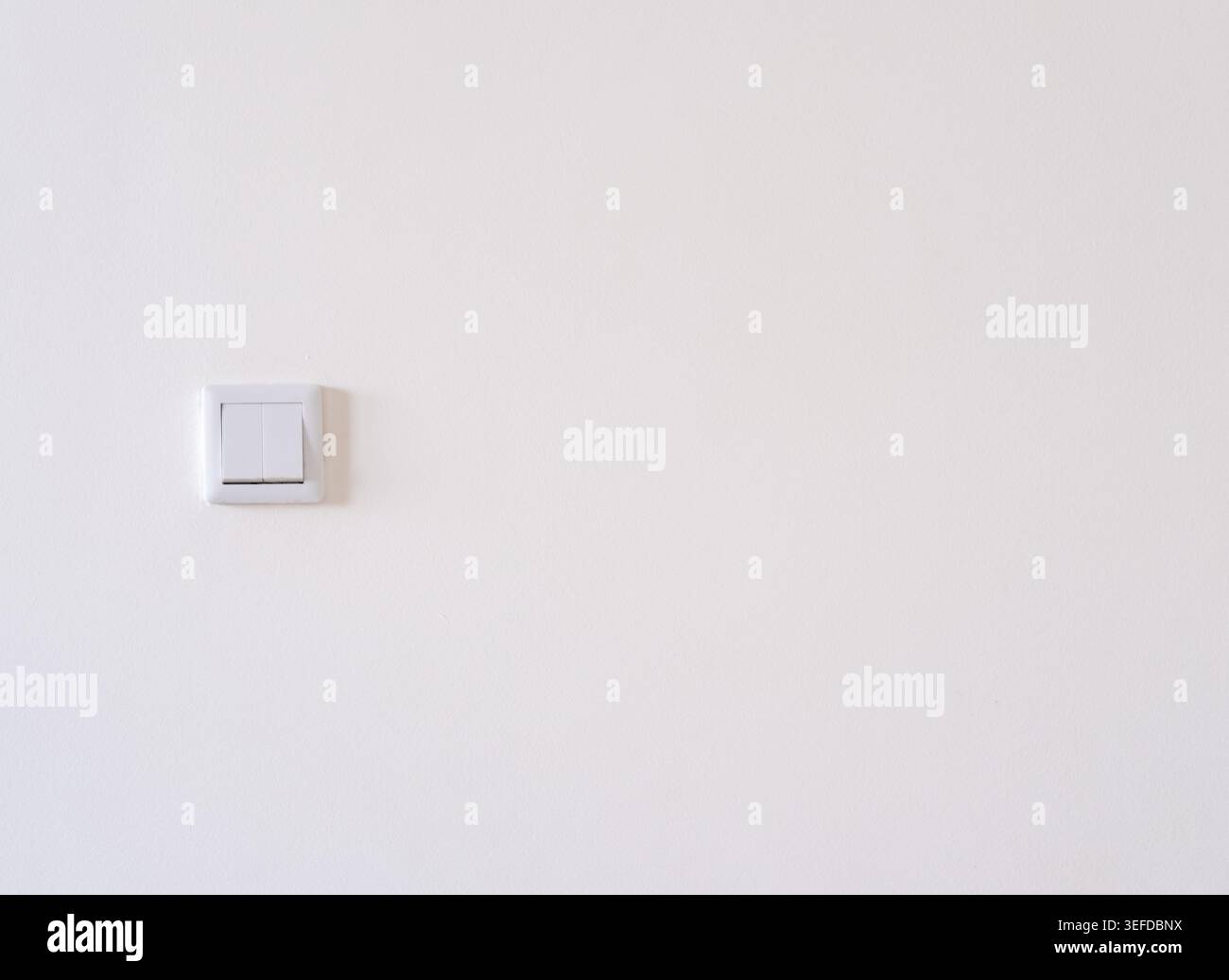 A white double rocker light switch is installed on a plain painted white wall Stock Photo