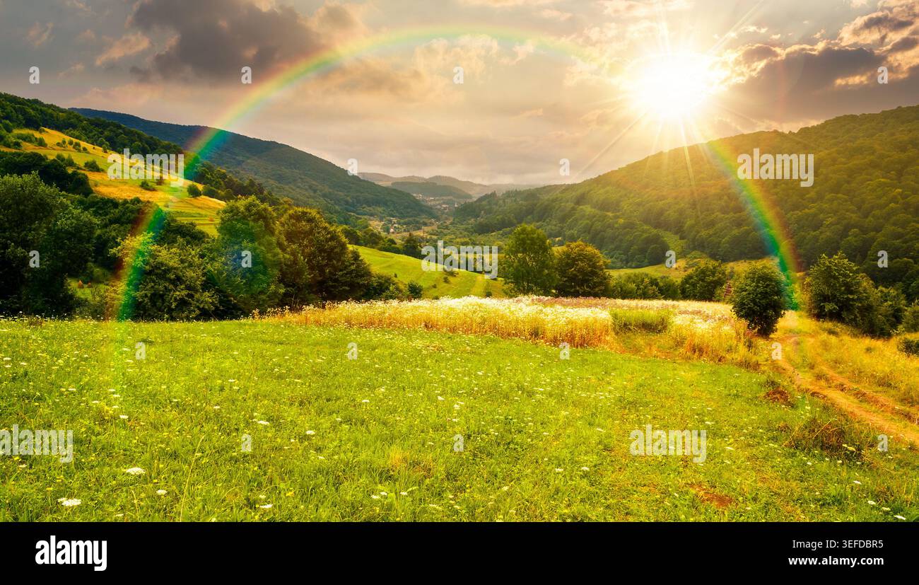 sunset over rural field on the hill. view in to the valley. countryside mountain landscape. alpine pasture near forested hills. timeless nostalgia boo Stock Photo