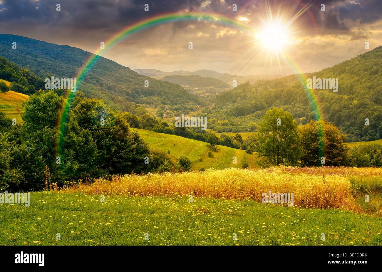 sunset over rural field on the hill. view in to the valley. countryside mountain landscape. alpine pasture near forested hills. timeless nostalgia boo Stock Photo