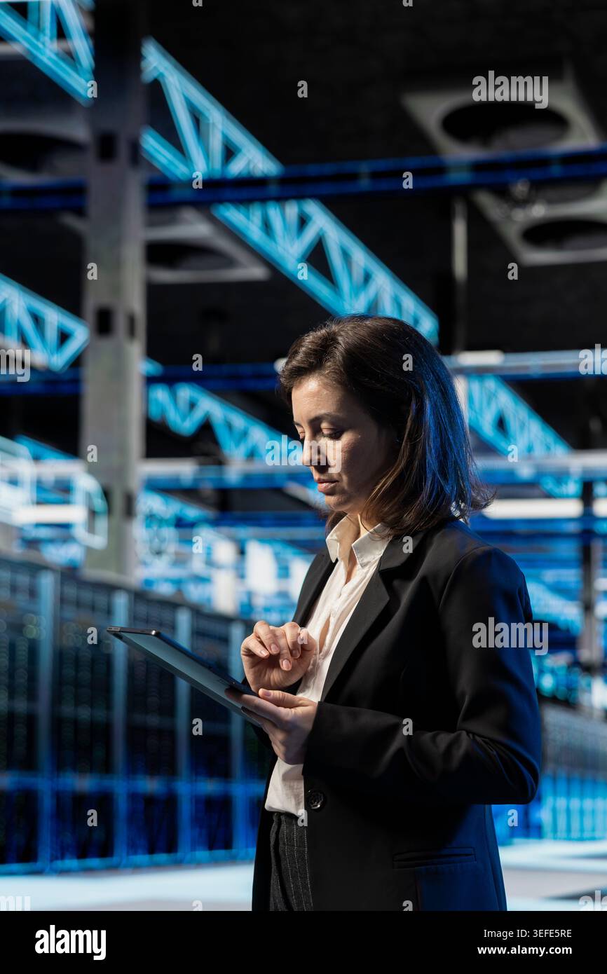Data center software developer using tablet to inspect infrastructure rackmounts, updating network systems. IT expert using device to ensure stable server room operations, overseeing equipment rigs Stock Photo