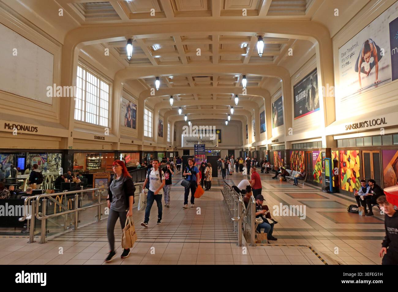 Busy Leeds City station interior showing retail units, ticket barriers and passengers beneath the historic concourse roof. Stock Photo