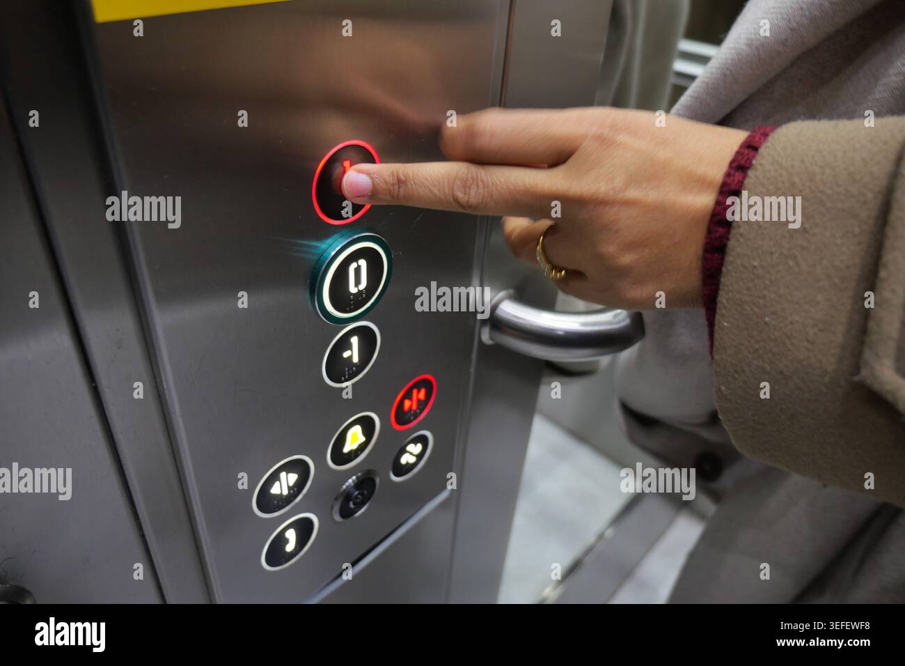 Person presses button in elevator at busy location Stock Photo