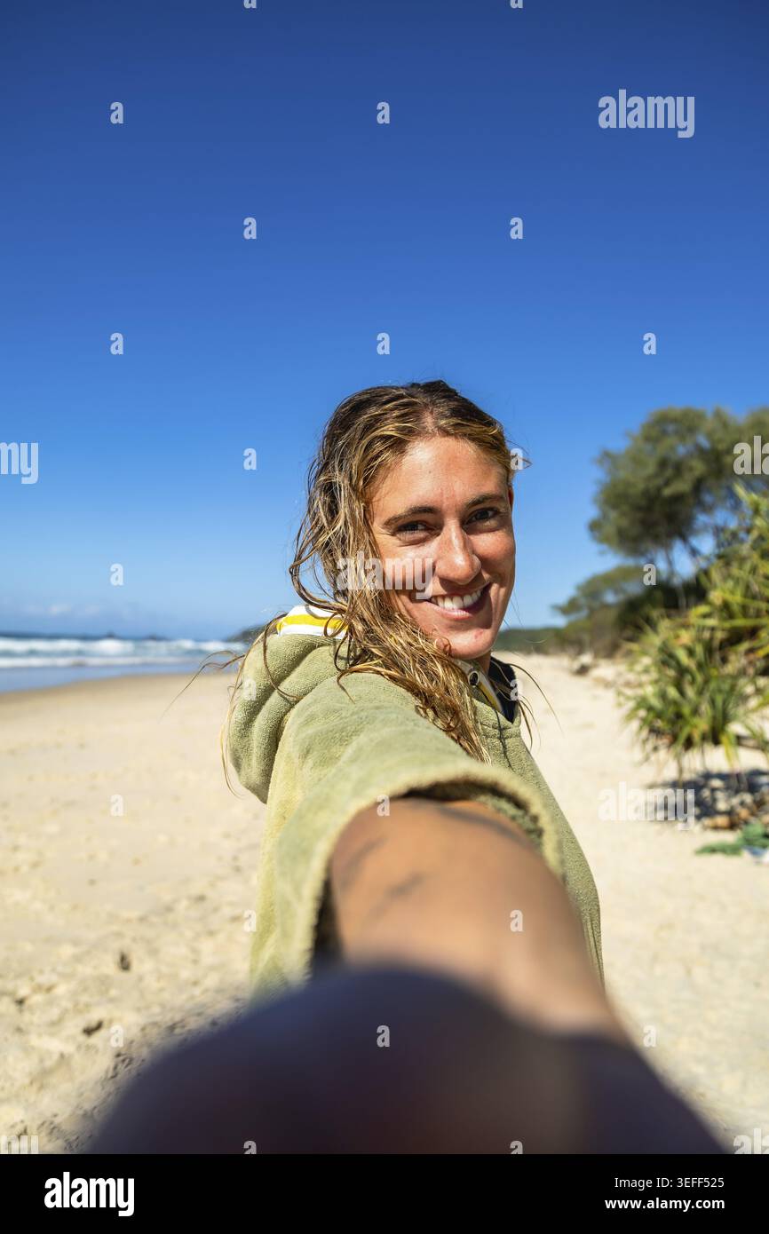 Woman smiling with wet hair after surfing on the gold coast, wearing a cozy poncho on a sunny beach day, enjoying ocean waves, sand, and relaxed summe Stock Photo