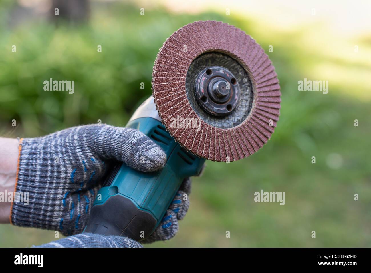 Professional handyman in protective gloves holds a powerful angle grinder with an abrasive flap disc. A concept of confidence, high productivity, and Stock Photo
