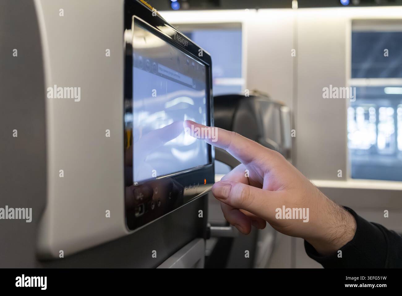 A close up of a human finger selecting content on a digital tablet screen mounted on a train seat highlights user interface interaction, wireless conn Stock Photo