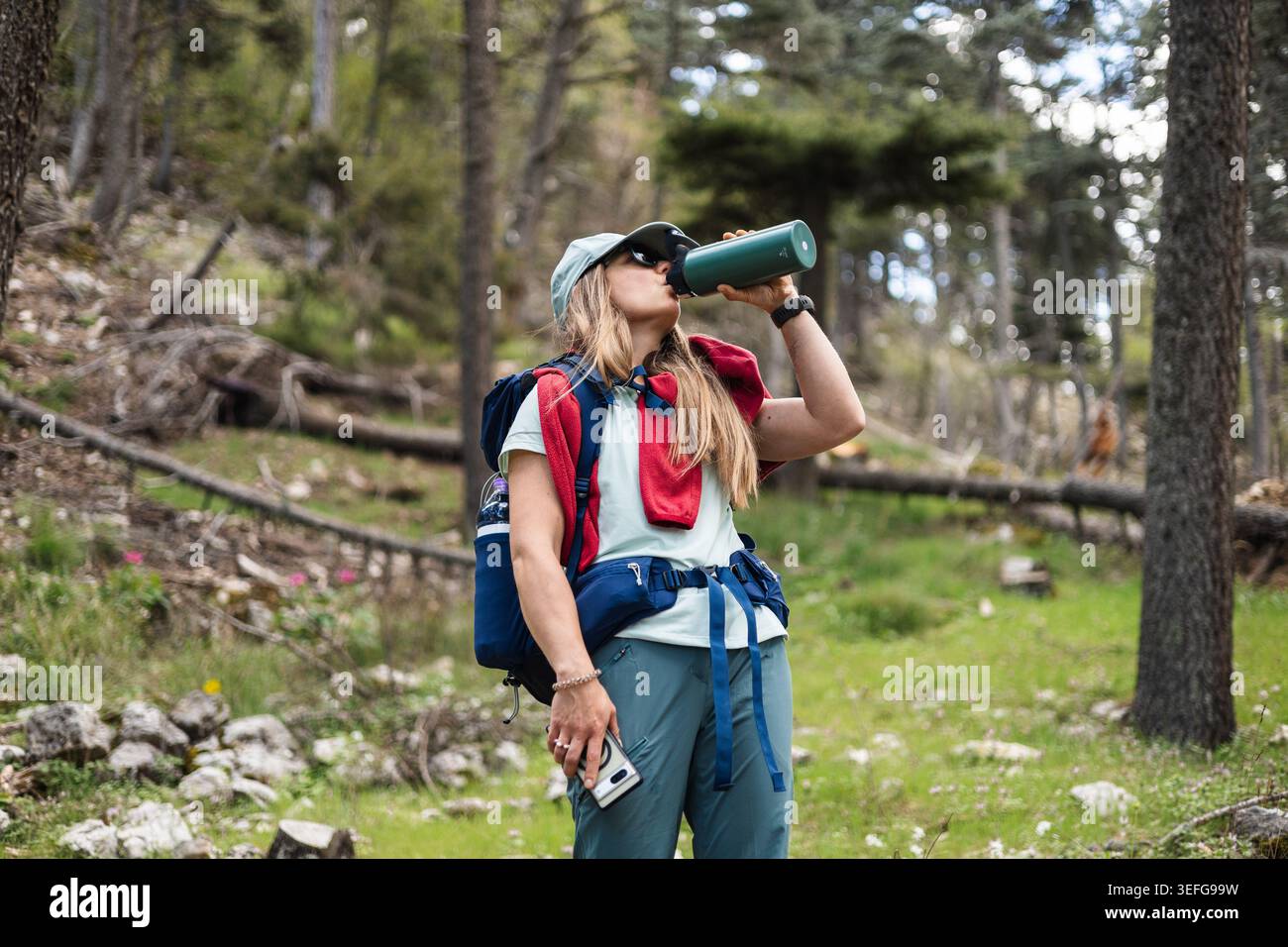 Young woman drinks from water bottle while hiking in forest Stock Photo