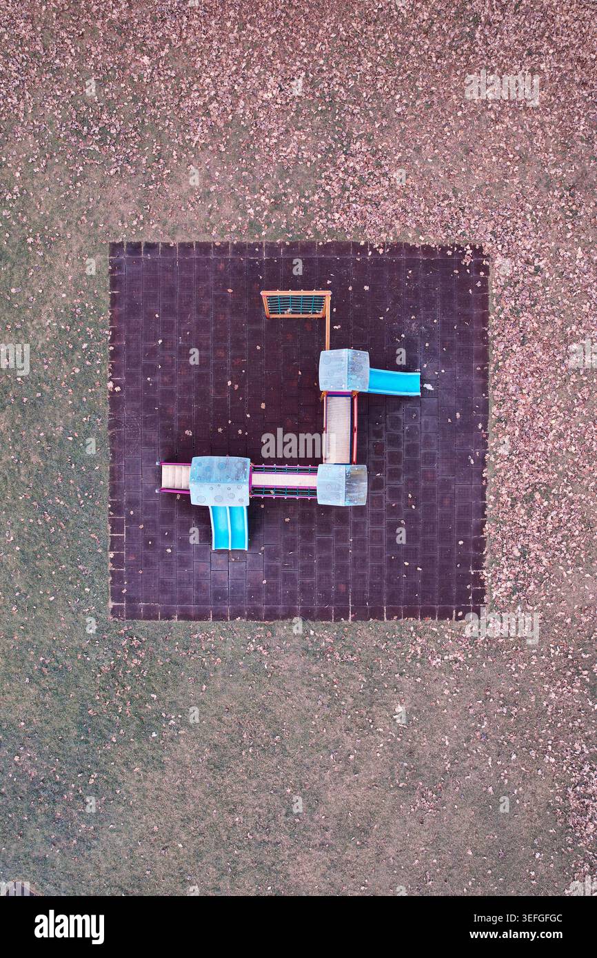 Aerial view of a colorful playground structure with blue slides on a dark square mat surrounded by autumn leaves in Turin, Piedmont, Italy. Stock Photo