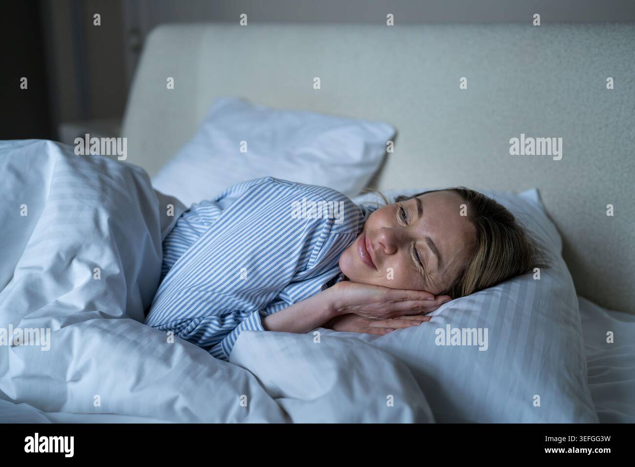 Happy serene mature woman lounging in cozy bed, awakening with smile, positive emotions, good mood. Stock Photo