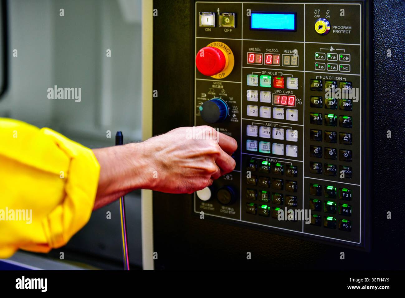 Operator hand adjusting dial knob on CNC machine control panel, industrial manufacturing concept. Stock Photo