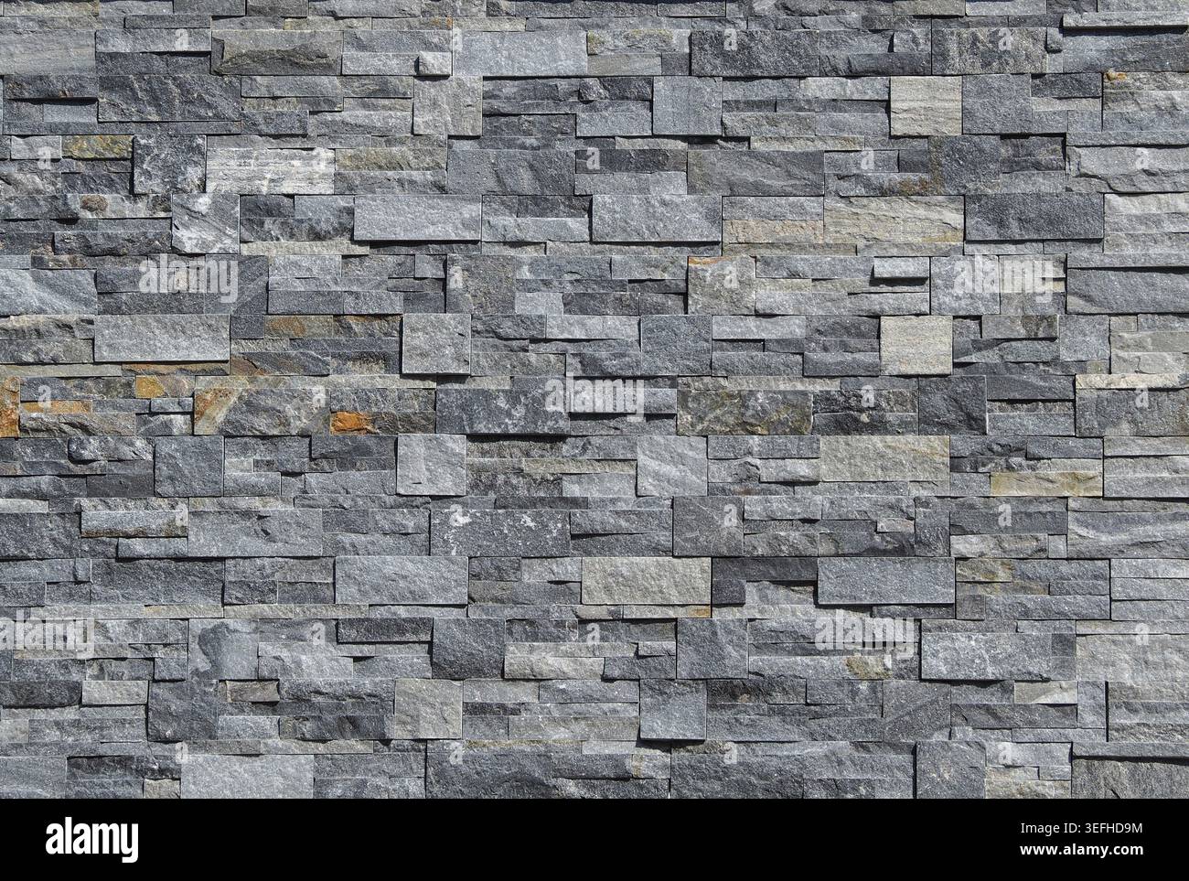 Grey stone wall cladding made of strips and square blocks stacked . Background and texture. Stock Photo