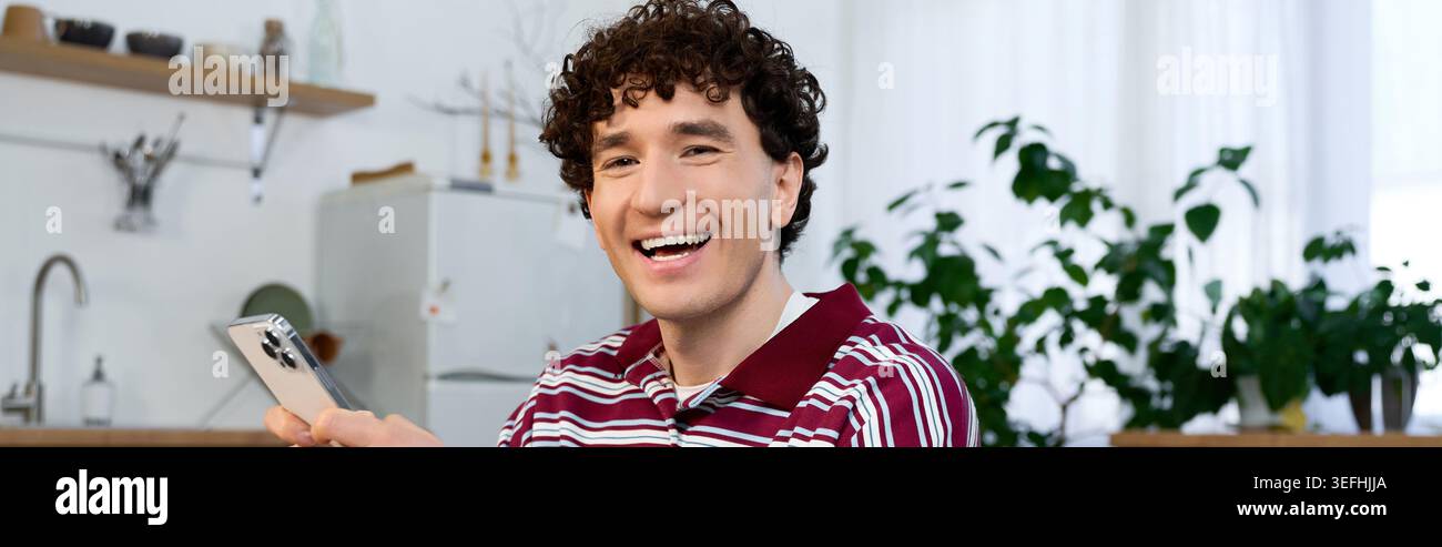 Young man with curly hair relaxes and smiles in his stylish apartment, banner Stock Photo