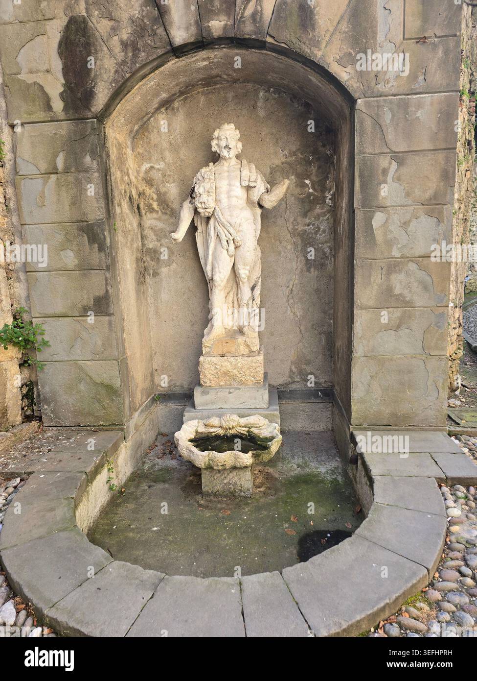 A weathered stone fountain with a classical figure in an arched niche in the historic streets of Bergamo Alta, Lombardy, Italy - Smartphone Captured Stock Image