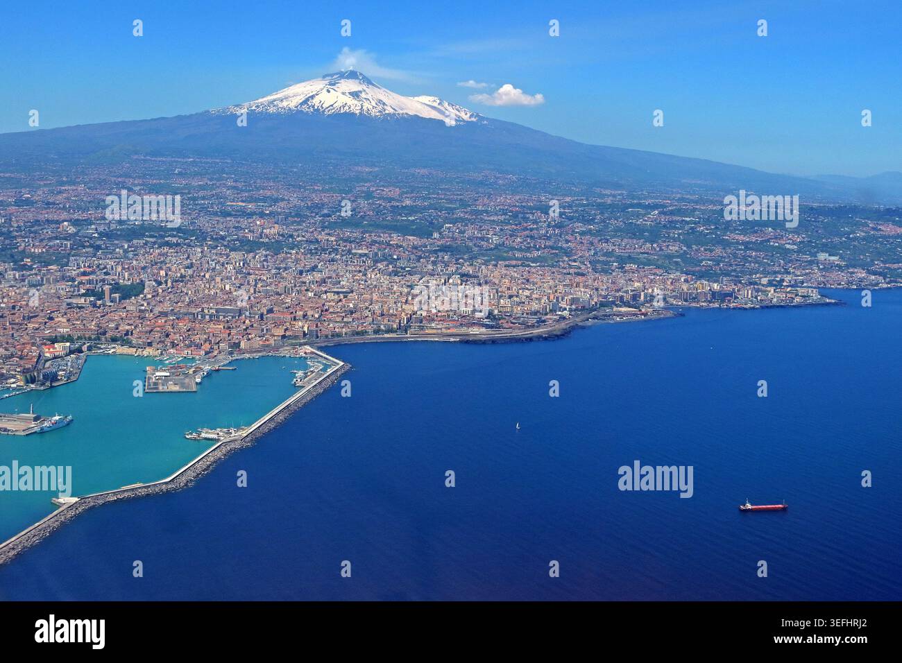 Catania port and city with snow-capped Mount Etna smoking in the background, Taormina , Sicily, Italy. Stock Photo