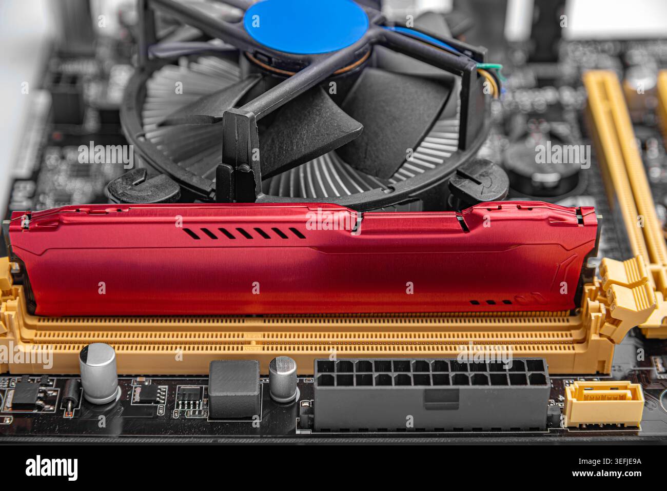 A RAM module installed on a computer motherboard next to a CPU cooling fan. Stock Photo